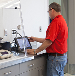 A man in a red shirt and jeans looks at a monitor in a testing laboratory.